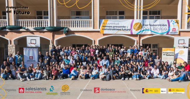 Foto grupal de participantes en un evento juvenil de Salesianos y Confederación Don Bosco, con banners que destacan colaboración y patrocinios